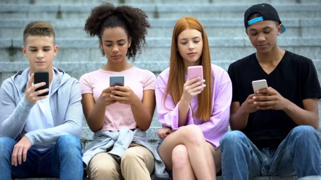 Adolescentes brancos e negros sentados em uma escada olhando para seus celulares