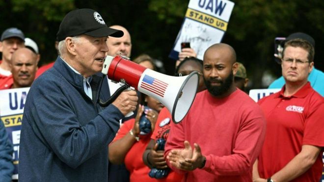 Biden discursando com megafone vermelho em piquete