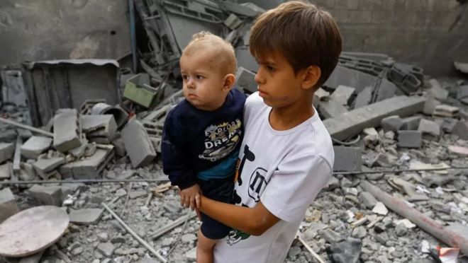 Hai em bé người Palestine đứng tại đống đổ nát tại Khan Younis, nam Dải Gaza