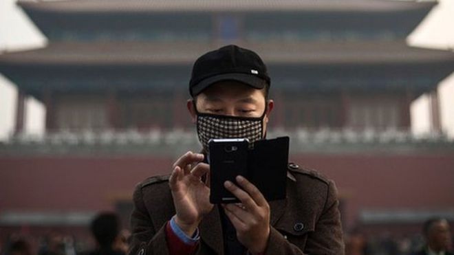 A Chinese man wears a mask to protect against pollution as he uses his smartphone on a hazy day outside the Forbidden City 20 November 2014 in Beijing, China