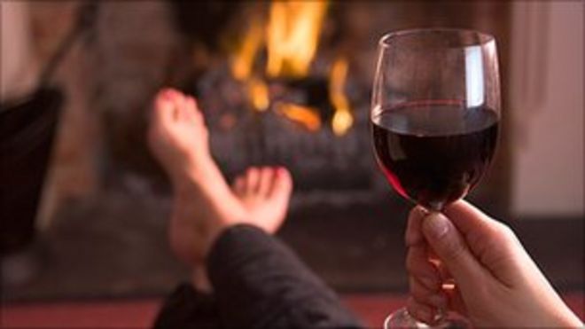 Человек, пьющий вино с поднятыми ногами перед огнем