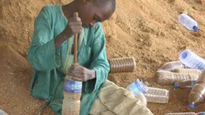 Ребенок в Yelwa упаковывает бутылки с песком