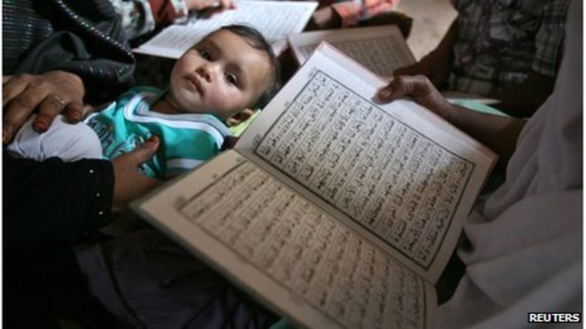 Оставшиеся в живых читают Коран, а ребенок смотрит во время празднования 10-й годовщины беспорядков Годры в западном индийском городе Ахмедабад 27 февраля 2012 г.
