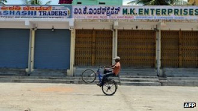 Индийский мальчик проезжает мимо закрытых магазинов во время общенациональной забастовки в Бангалоре