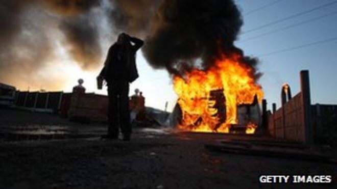 Активист смотрит перед горящим караваном, который был подожжен активистами, чтобы использовать его как баррикаду, поскольку выселения начинаются в лагере путешественников на ферме Дейл