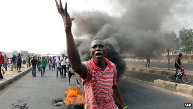 Протестующий перед горящей шиной в Лагосе, Нигерия (январь 2012 г.)