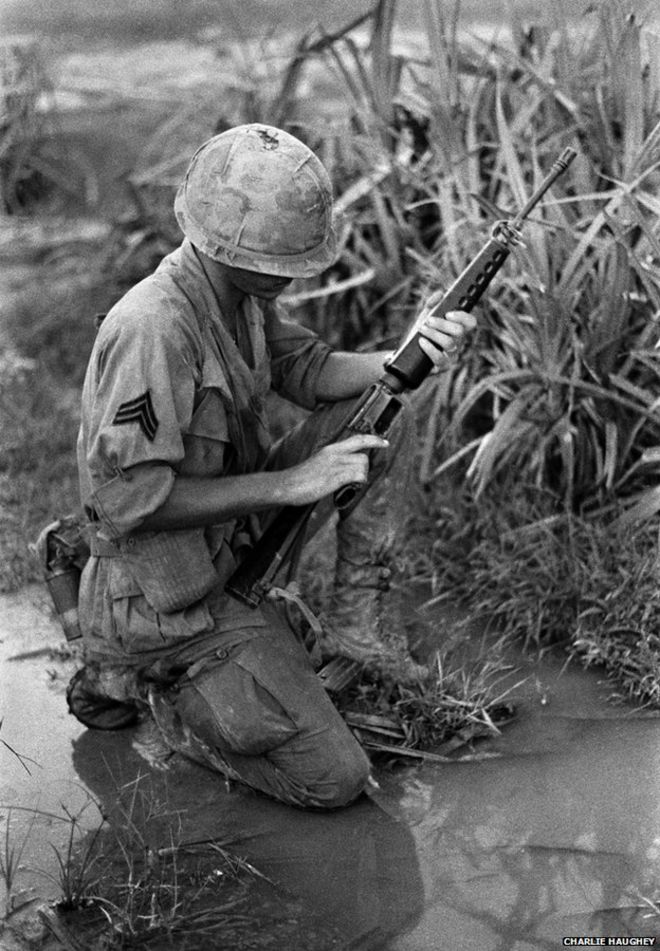 Сержант опускается на колени на мокрой земле и проверяет свой М16