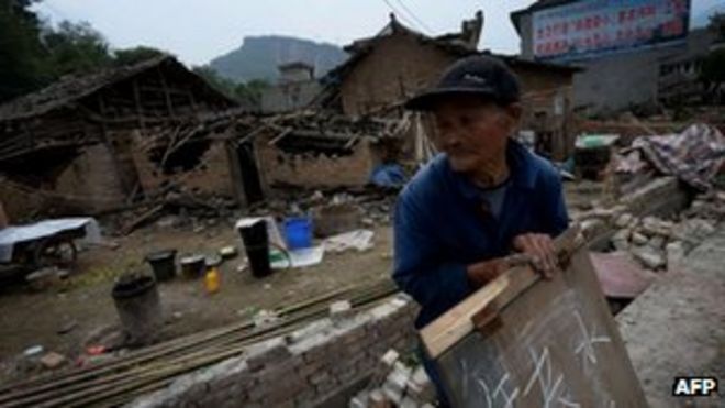 Пожилой мужчина держит табличку с просьбой о помощи возле своего разрушенного дома в деревне Лунмэнь после 7-й величины.Землетрясение 0 обрушилось на Лушань, провинция Сычуань, 22 апреля 2013 г.