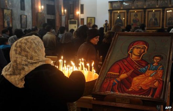 Сирийская женщина зажигает свечи, когда она посещает мессу в православной церкви Мар Элиас (Святой Илия) в Баб Тума, Дамаск (24 декабря 2012 года)