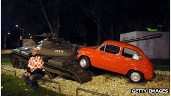 Музейная экспозиция танка, разбивающего маленький автомобиль, изображающий сцену войны за независимость Хорватии