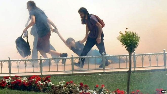 Демонстранты помогают друг другу, поскольку турецкие омоновцы используют слезоточивый газ для разгона столкновений (31 мая 2013 г.)