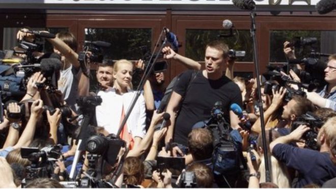 Лидер российской оппозиции Алексей Навальный (в центре) беседует со СМИ, а его жена Юлия (в центре) стоит неподалеку от здания суда в Кирове