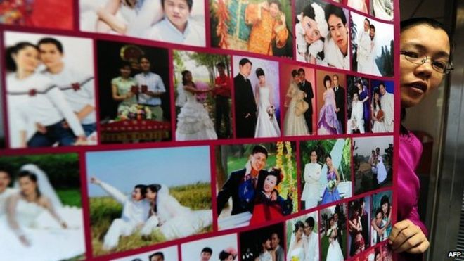 Гонг Хайян позирует возле плаката в своем пекинском офисе с фотографиями супружеских пар, которые встречались на ее сайте (фото из архива)