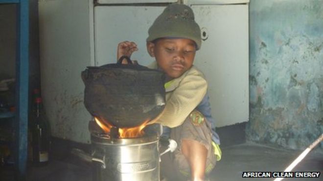 Маленький мальчик сидит рядом с бездымной печью, изготовленной компанией African Clean Energy в Лесото