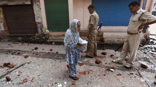 An elderly woman walks on a road scattered with bricks and stones during a communal clash in Muzaffarnagar