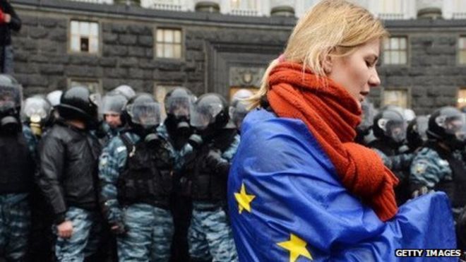 Украинская женщина, накинутая на флаг ЕС, стоит перед ОМОНом во время демонстраций в Киеве 25 ноября.