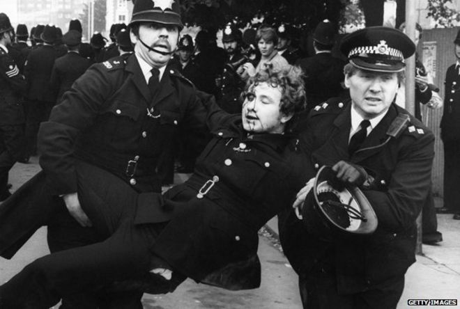 Полицейские увозят раненого коллегу из-за беспорядков в Льюишаме в 1977 году