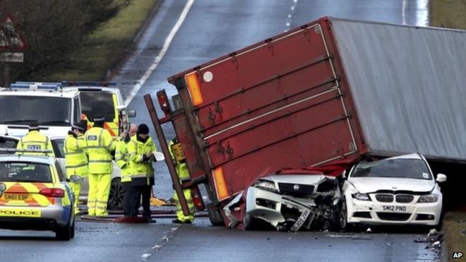 Аварийные работники присутствуют на месте происшествия со смертельным исходом грузовика, когда грузовик сидит на двух автомобилях возле Батгейта, Шотландия