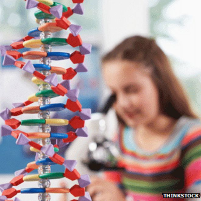 Девушка с помощью микроскопа с моделью ДНК на переднем плане