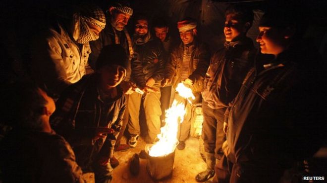 Сирийские беженцы собираются у пожара в лагере сирийских беженцев в ливанском пограничном городе Арсал (13 декабря 2013 года)