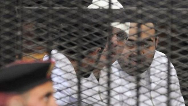 Политические активисты Ахмеда Махера, Ахмеда Дума (слева) и Мохамеда Аделя (справа) из движения 6 апреля смотрят из-за решеток в суд Абдина в Каире, 22 декабря 2013 года.