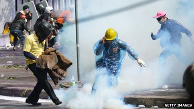 Антиправительственные демонстранты спешат накрыть канистру со слезоточивым газом во время яростной акции протеста на спортивном стадионе, где Избирательная комиссия Таиланда регистрирует кандидатов на предстоящий опрос в Таиланде в Бангкоке, Таиланд, 26 декабря 2013 г.
