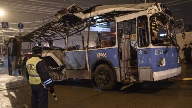 Милиционер наблюдает, как в Волгограде буксируется автобус, разрушенный в результате очевидного теракта, совершенного ранее в понедельник