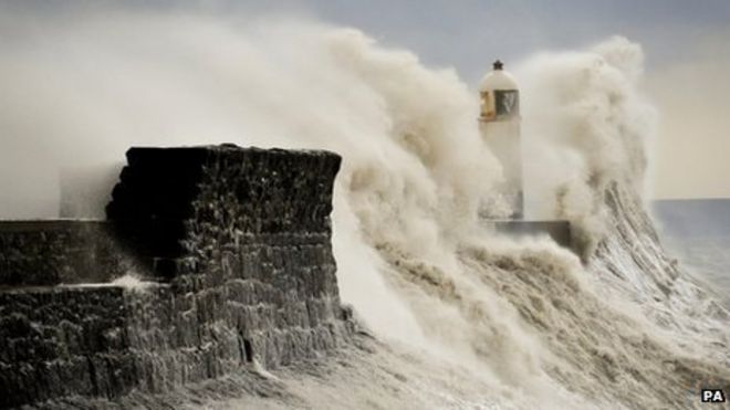 Огромные волны разбиваются о стену гавани и охватывают маяк в Портскале