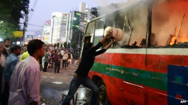 Житель Бангладеш 2 января 2014 года бросает воду в горящий автобус в Дакке.