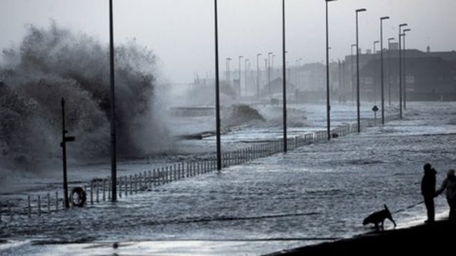 Волны катятся по морской стене и затопляют путь за ней