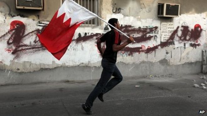 Бахрейнский антиправительственный демонстрант бежит с национальным флагом во время столкновений с полицией по охране общественного порядка, стреляющей слезоточивым газом в Санабисе, Бахрейн, 18 октября 2013 г.