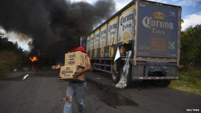 Мародер несет коробки с пивом, так как грузовик Corona горит на блокпосту, предположительно установленном последователями картеля рыцарей-тамплиеров в Тьерра-Кальенте 10 января 2014 года
