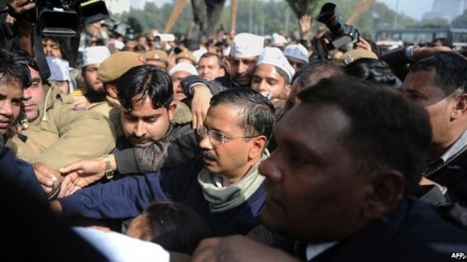 Главный министр Нью-Дели Арвинд Кейривал (C) окружен полицейскими и людьми, которые его защищают, когда он пробирается сквозь толпу сторонников и СМИ во время акции протеста на улицах Нью-Дели 20 января 2014 года