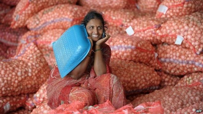 Индийские рабочие говорят по сотовому телефону, когда она сидит на луковых пакетиках