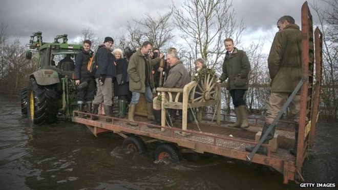 Принц Чарльз сидит на тракторном прицепе, когда он посещает пострадавшую от наводнения деревню Мучелни