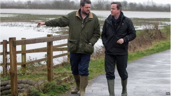 Дэвид Кэмерон говорит с фермером Тимом Хуком, когда они идут по дороге рядом с затопленной землей