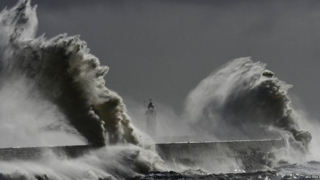 Большие волны обрушиваются на маяк и гавань во время прилива в Ньюхейвене в Сассексе