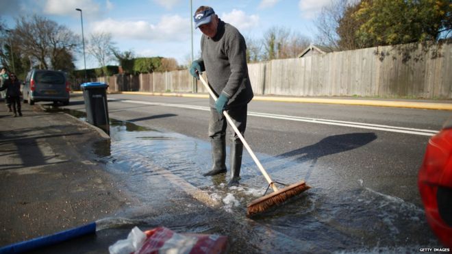 Мужчина пытается отмыть паводков от передней части своего дома в Чертси, Англия
