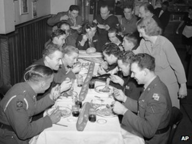 Анита О'Мера, из персонала столовой «Сцена», подает вино солдатам армии США, флота и канадской армии, в то время как Джо, босс рук Колуччи, разносящих спагетти и пиццерию в Нью-Йорке 26 декабря 1942 г.