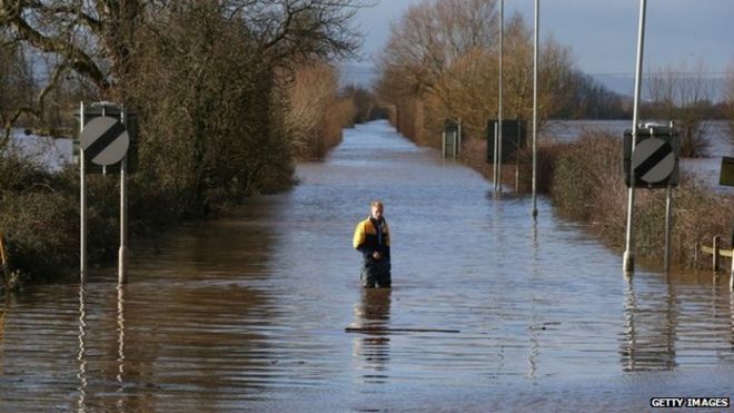 Мужчина стоит в паводковой воде на A361 в Burrowbridge на Сомерсетских уровнях 10 февраля