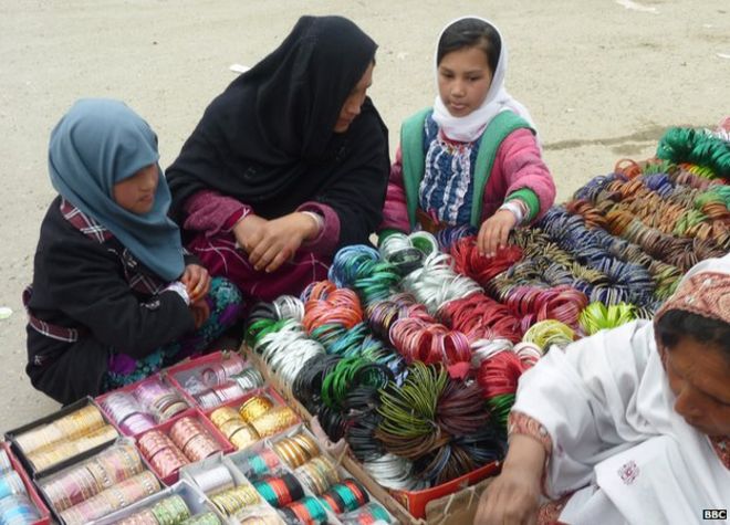 Женщина и две молодые девушки осматривают прилавок, в котором продаются яркие цветные браслеты