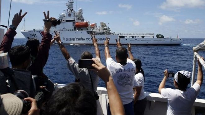 Филиппинские морские пехотинцы и местный телевизионный репортер (L) указывают на судно береговой охраны Китая в Южно-Китайском море 29 марта