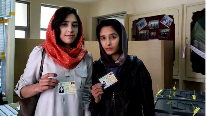 Две молодые женщины-избиратели показывают свои удостоверения личности на избирательном участке в Кабуле