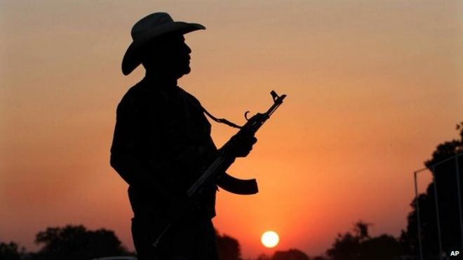 Неизвестный вооруженный человек из группы боевиков стоит с оружием у входа в Апацинган в Мичоакан 9 февраля 2014 года