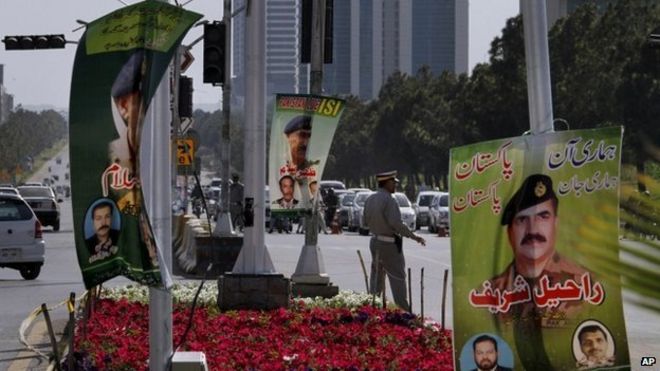 Офицер полиции контролирует движение возле плаката с изображением начальника межведомственной разведки Пакистана, генерал-лейтенанта Захира Ислама, в центре, который выставляют торговцы на главных дорогах, чтобы показать свою поддержку пакистанской армии и ISI в Исламабаде, Пакистан (26). Апрель 2014)