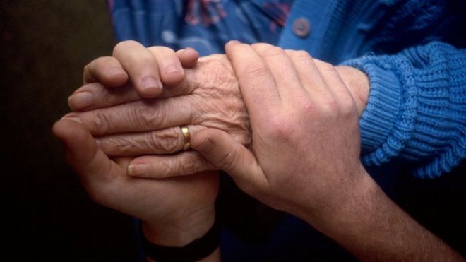 Опекун держит за руку пожилую женщину
