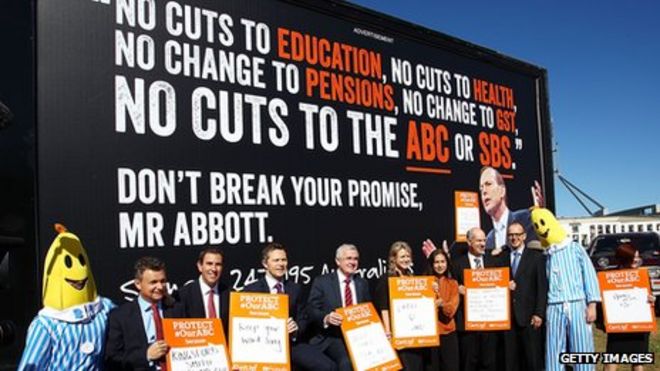 Министры и сенаторы позируют для СМИ перед рекламным щитом с изображением премьер-министра Тони Эбботта на митинге ABC возле здания парламента 13 мая