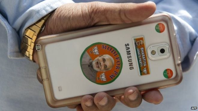 Рабочий BJP держит смартфон, украшенный наклейками с изображением главного министра западно-индийского штата Гуджарат и кандидата в премьер-министры главной оппозиционной партии Bharatiya Janata (BJP) Нарендры Моди в головном офисе партии в Нью-Дели.
