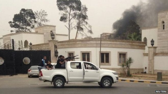 Вооруженные люди направляют свое оружие из автомобиля, когда дым поднимается на заднем плане возле Всеобщего национального конгресса в Триполи 18 мая