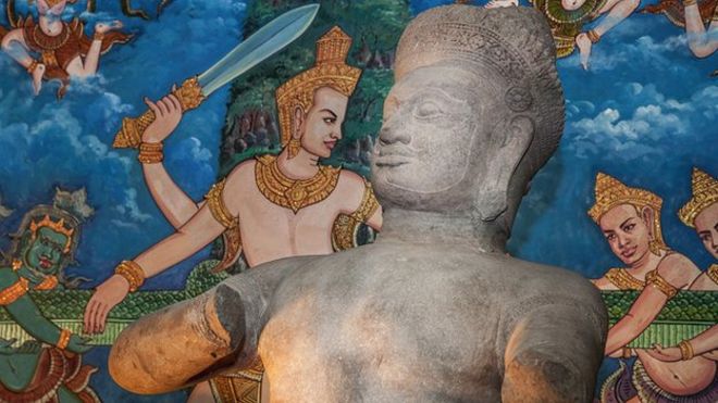 Статуя Бхима показана перед картиной, изображающей барельеф Ангкор-Вата, изображающий вспенивание Молочного моря во время церемонии передачи трех статуй обратно в Камбоджу на Совете министров 3 июня 2014 года в Пномпене, Камбоджа